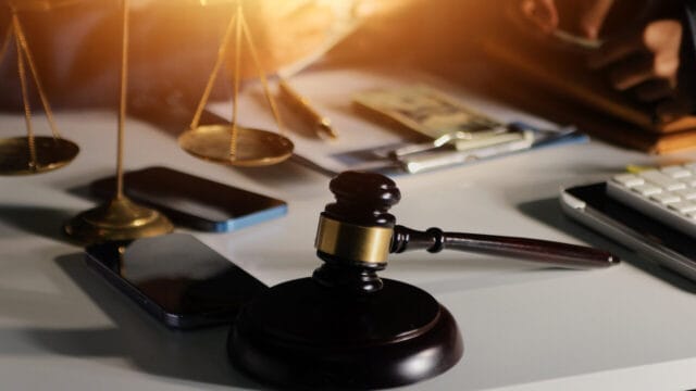 Brass scales, gavel, smartphone and calculator laid out on a desk in warm light