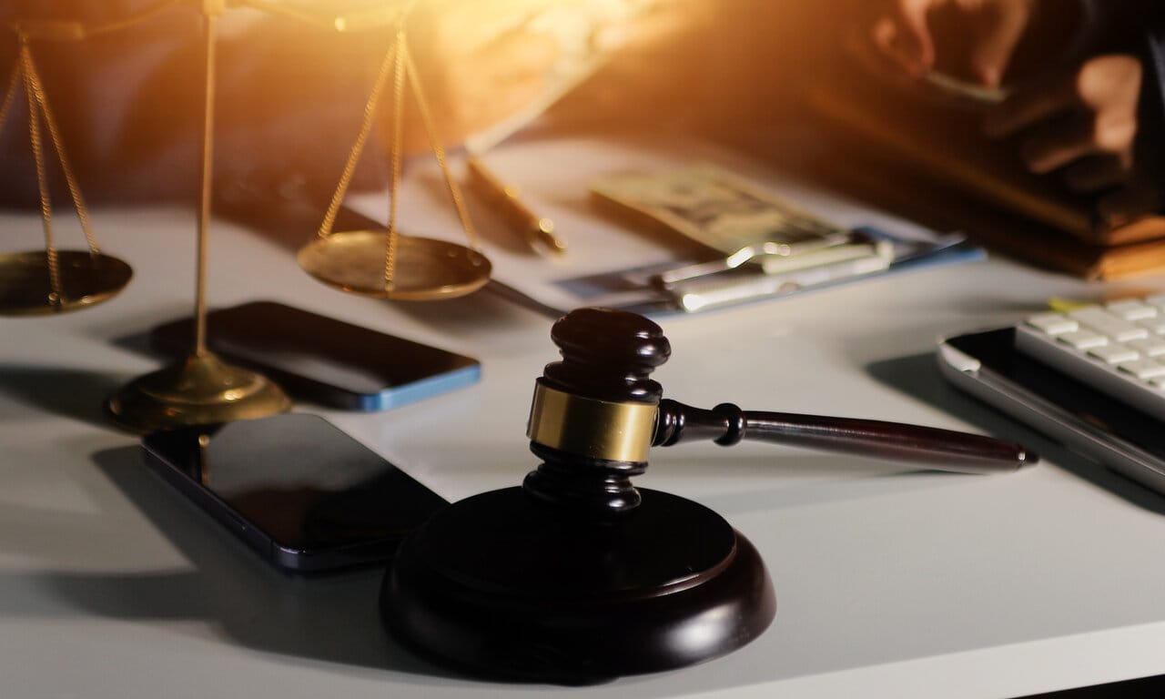 Brass scales, gavel, smartphone and calculator laid out on a desk in warm light