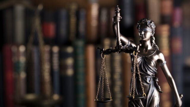 Bronze Lady Justice figurine with scales in front of a shelf of worn law books