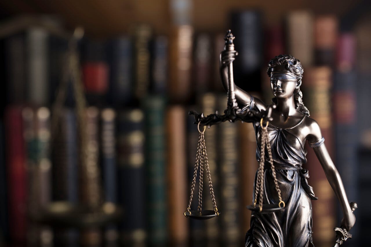 Bronze Lady Justice figurine with scales in front of a shelf of worn law books