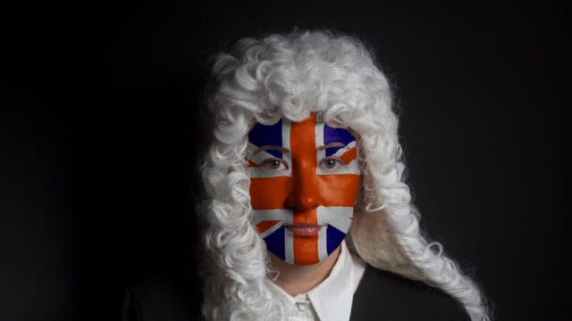 Portrait of a person in a traditional white judicial wig with a flag painted across the face