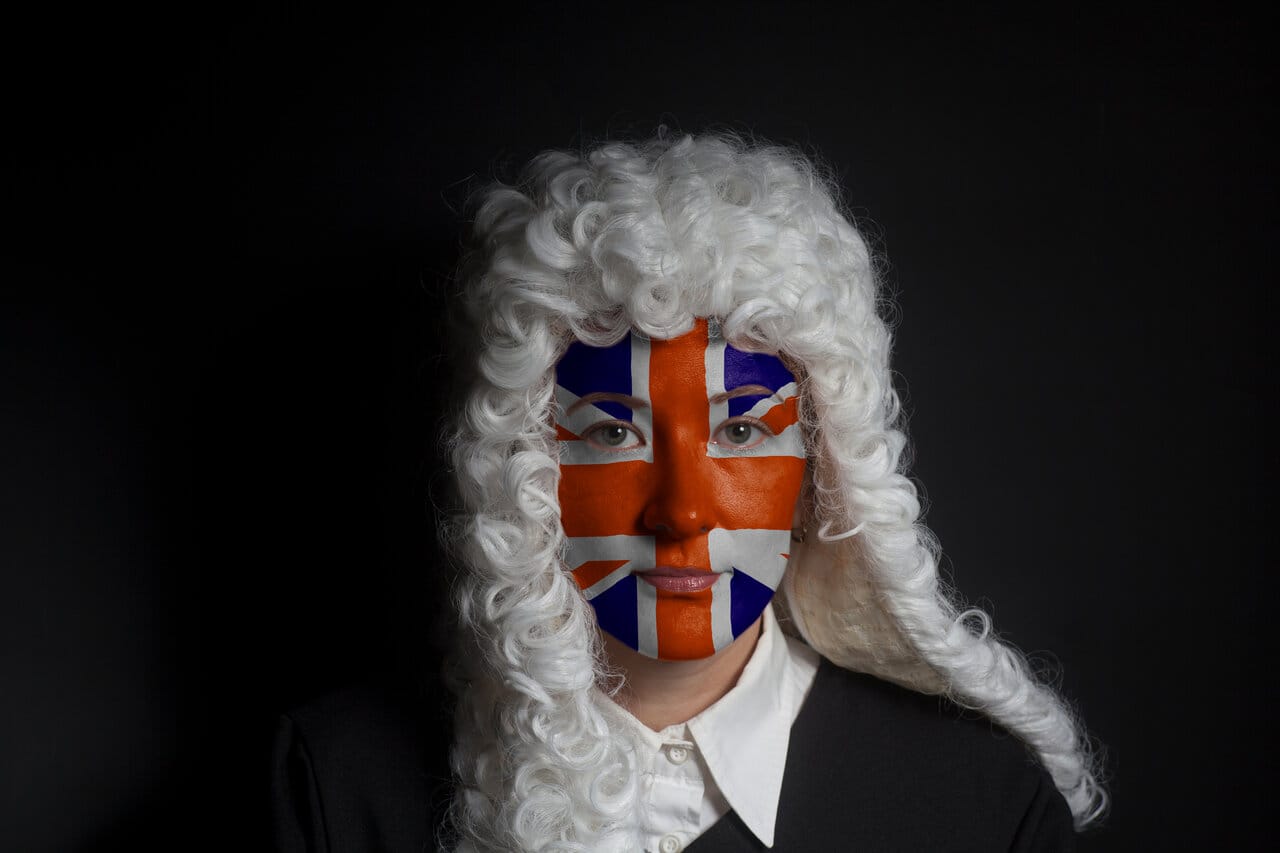 Portrait of a person in a traditional white judicial wig with a flag painted across the face