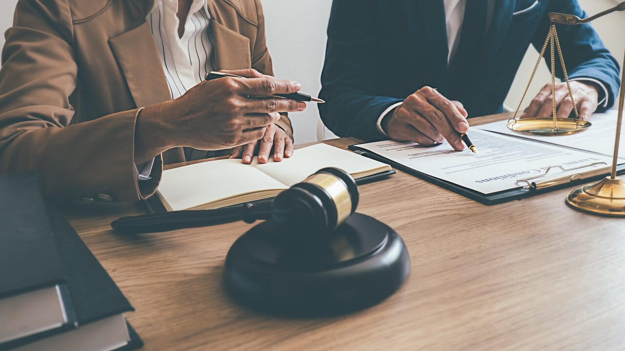 Two people reviewing a contract at a desk with a gavel and brass scale between them