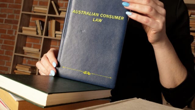 Person holding a blue consumer-law volume in front of library shelves