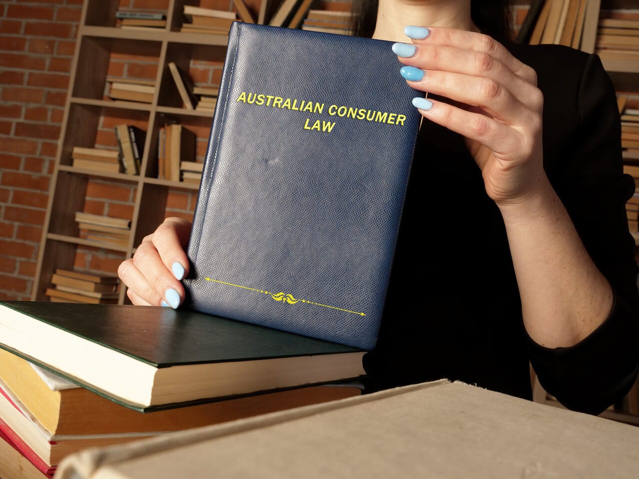 Person holding a blue consumer-law volume in front of library shelves