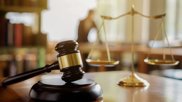 Gavel beside twin brass scales on a wooden table in a law library
