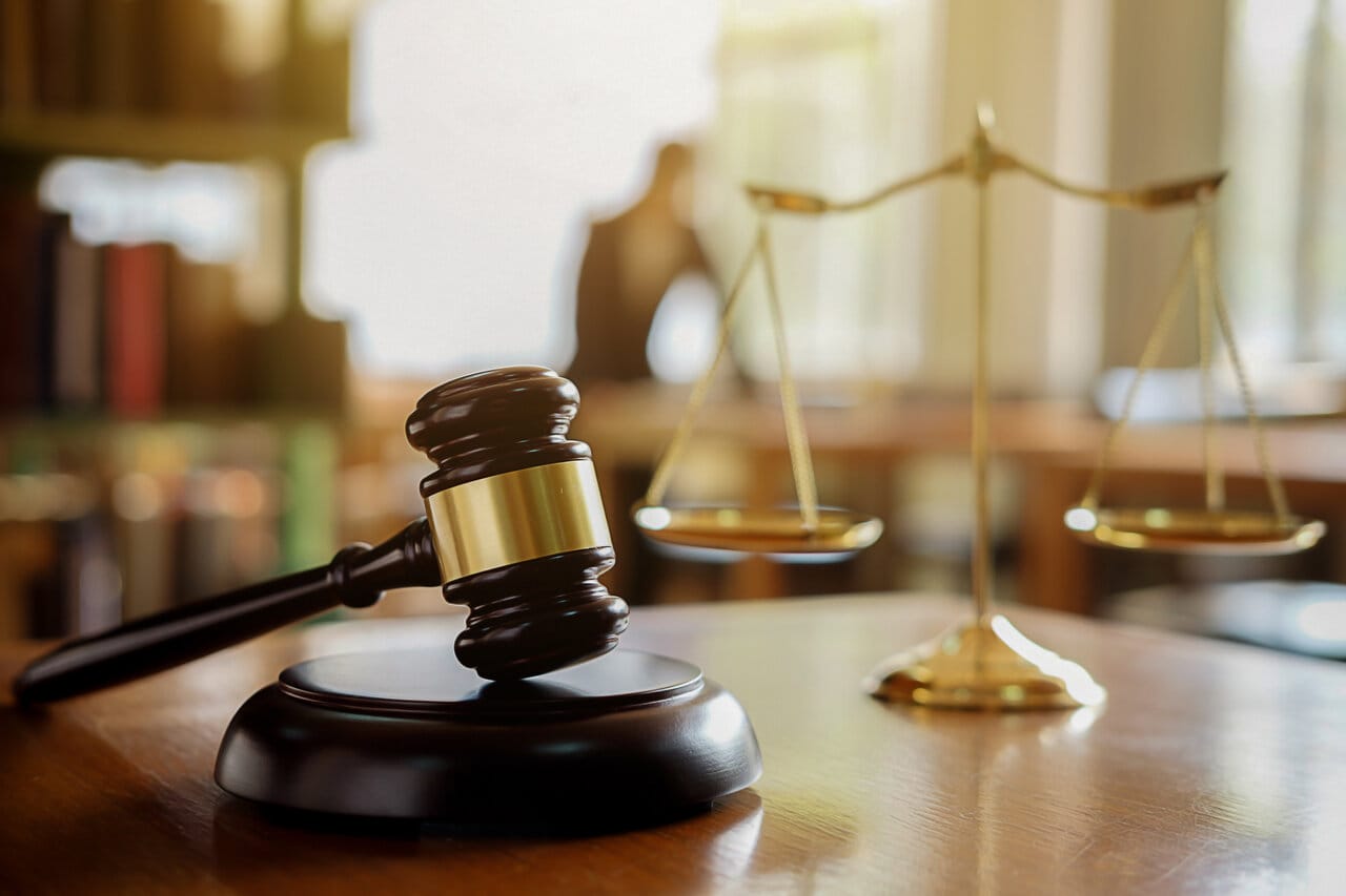 Gavel beside twin brass scales on a wooden table in a law library