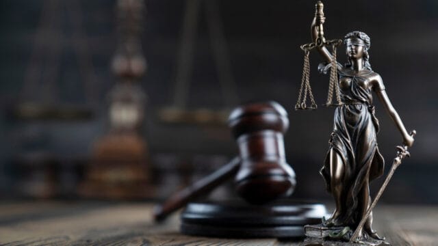 Dark close-up of a wooden gavel beside a Lady Justice statuette