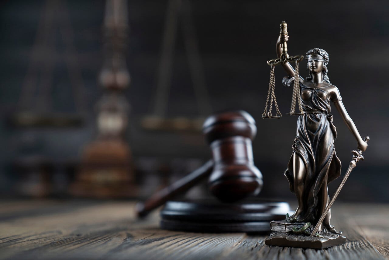 Dark close-up of a wooden gavel beside a Lady Justice statuette